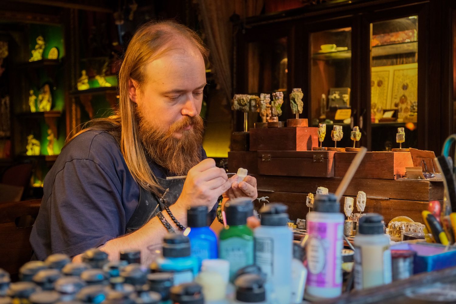 An artisan carefully crafting miniatures at a hobby workbench with sculpting tools and resin models visible