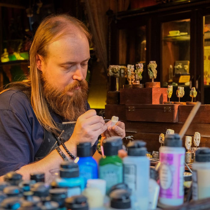 An artisan carefully crafting miniatures at a hobby workbench with sculpting tools and resin models visible